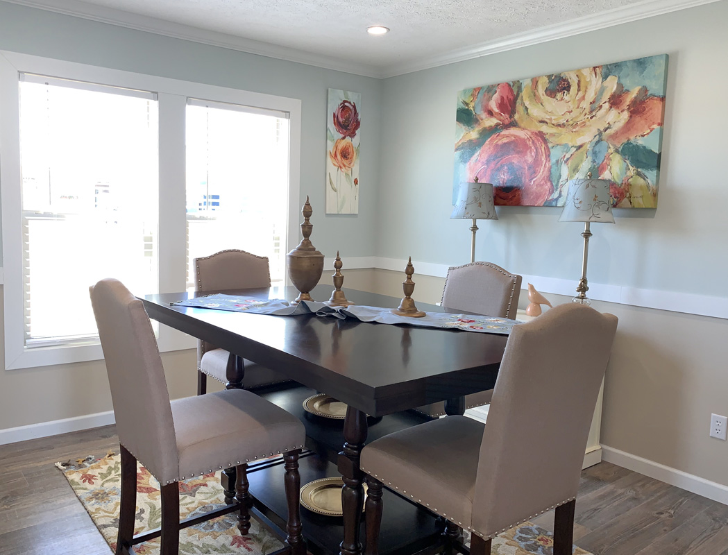 A dining room with a dark wood table and four beige upholstered chairs. Bright floral paintings and soft lighting create a warm, inviting atmosphere.