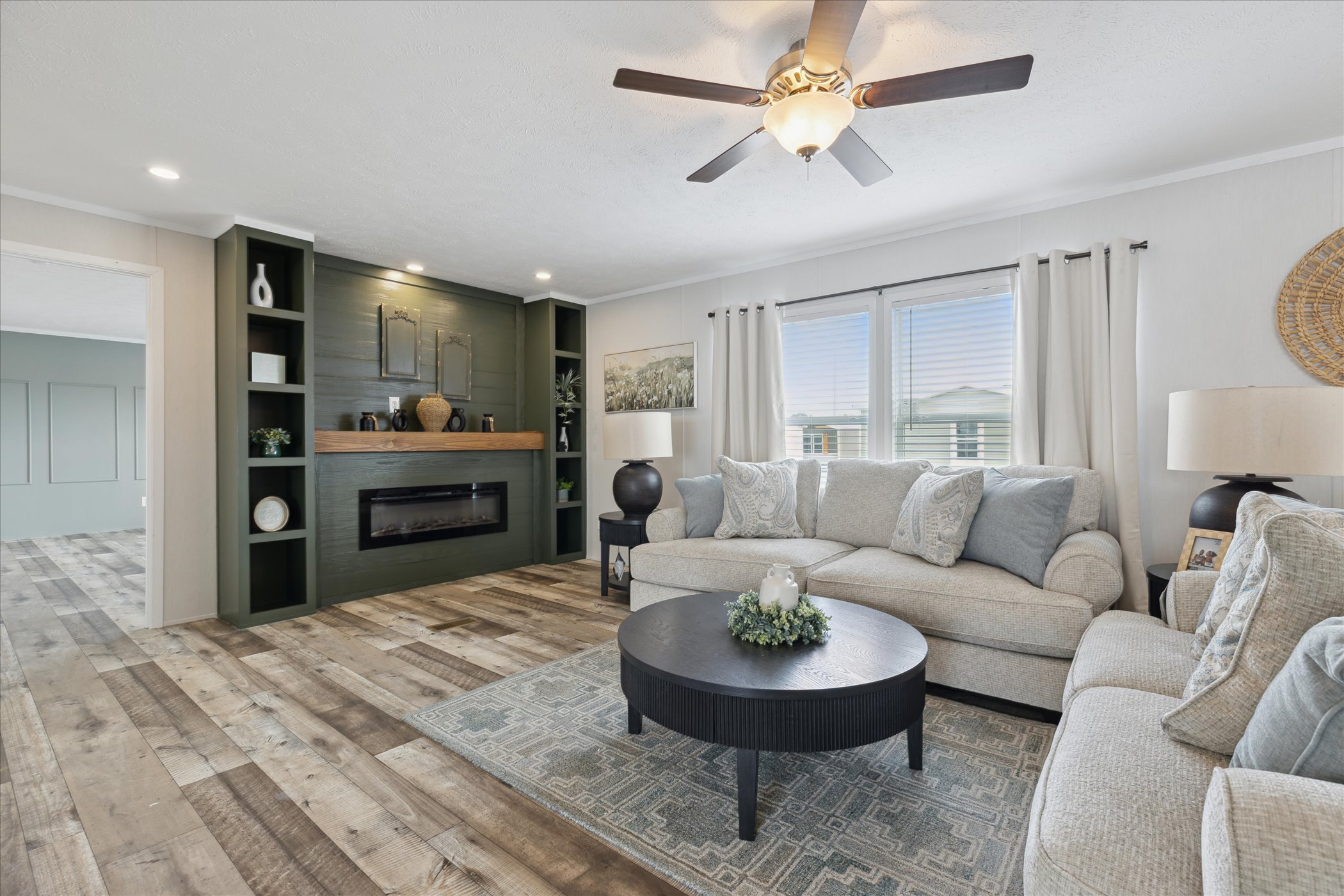 A cozy living room with light gray sofas, a round black coffee table, and a green paneled fireplace. Soft lighting creates a serene, welcoming atmosphere.
